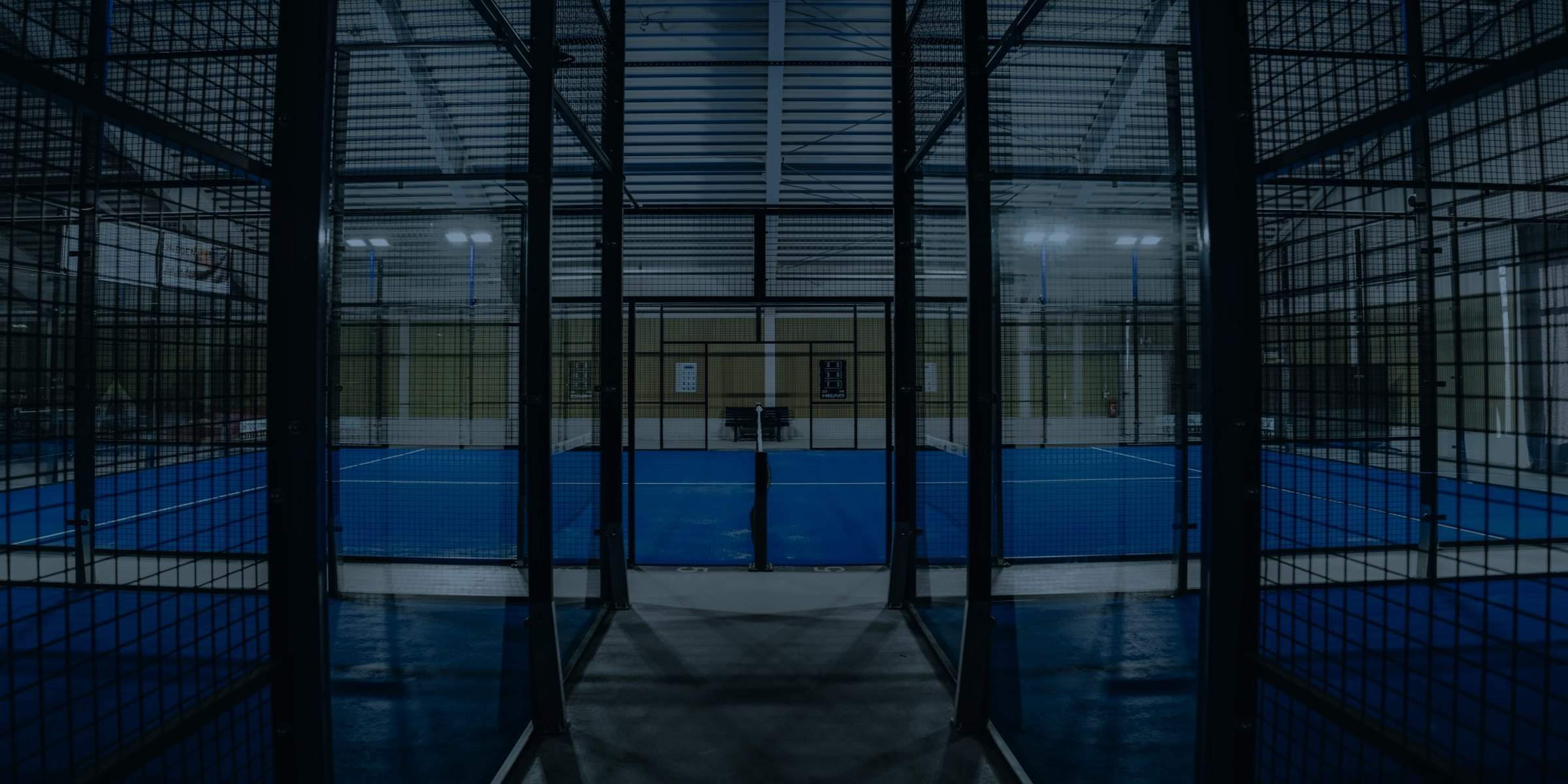 View between two courts into a padel hall under floodlights