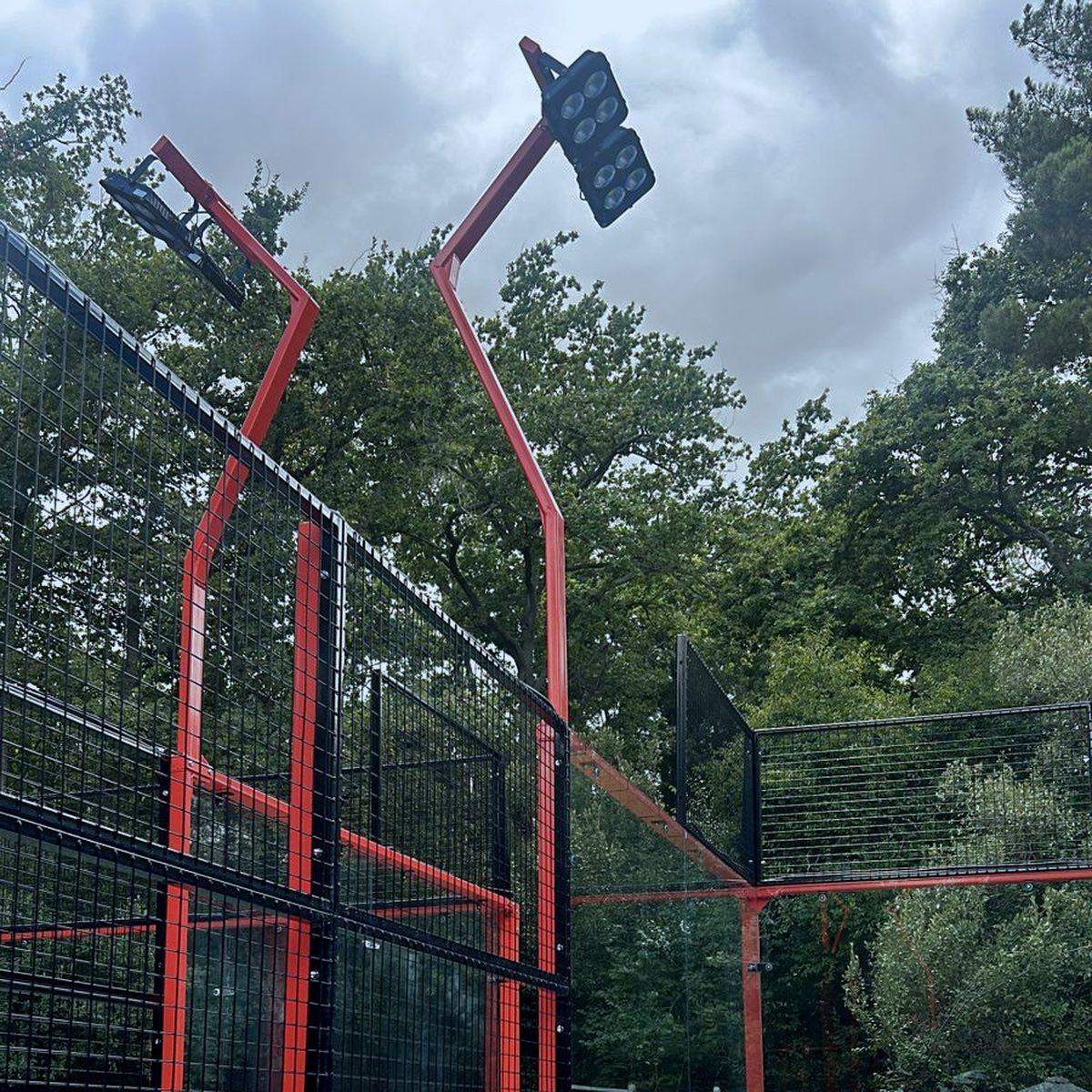 Zwei gebogene rote Lichtmasten mit LED-Flutern über einem Padel Court