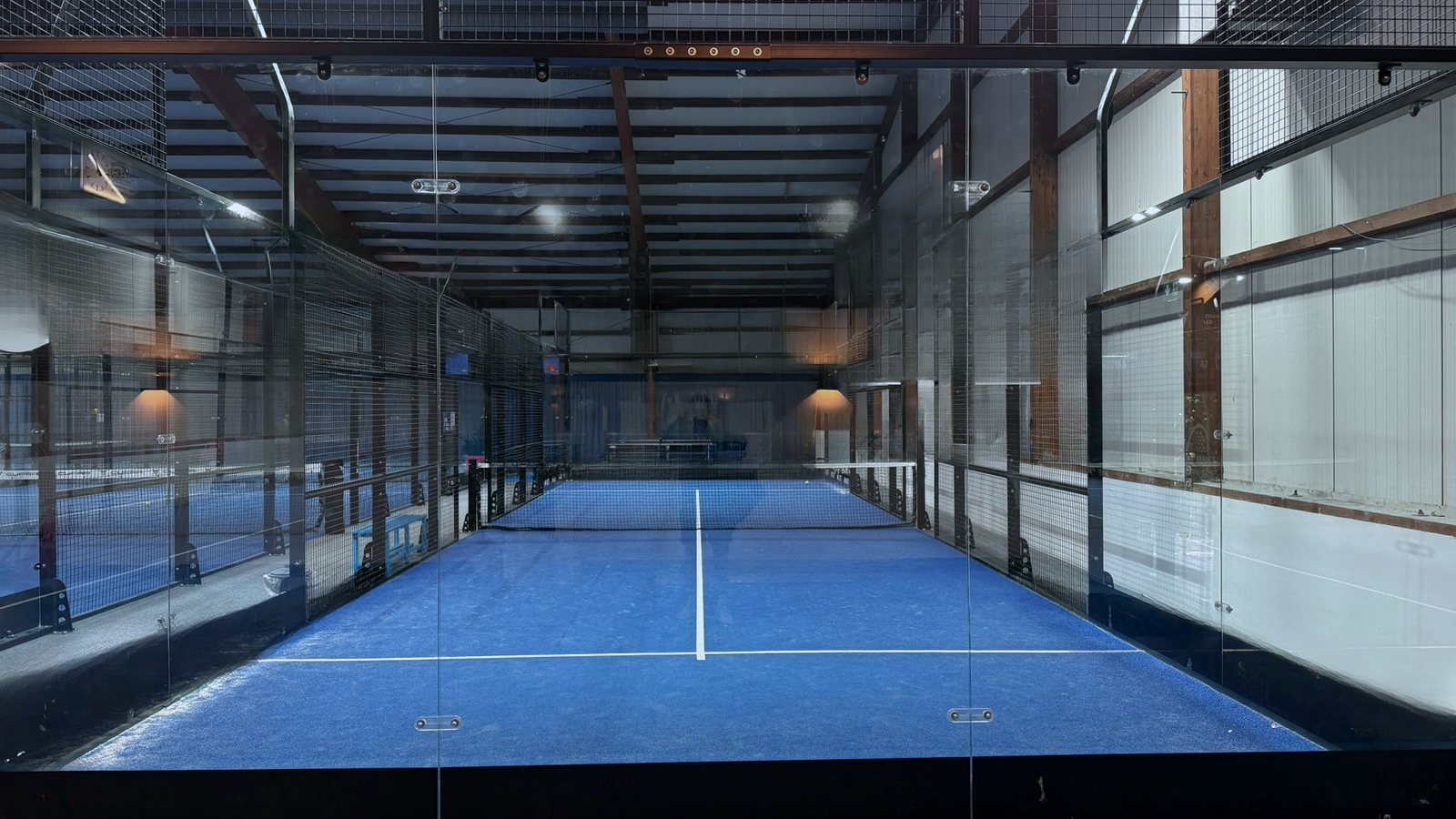 Installierter Single Padel Court durch die Glasrückwand gesehen, blauer Kunstrasen und Gitterfelder an den Längsseiten