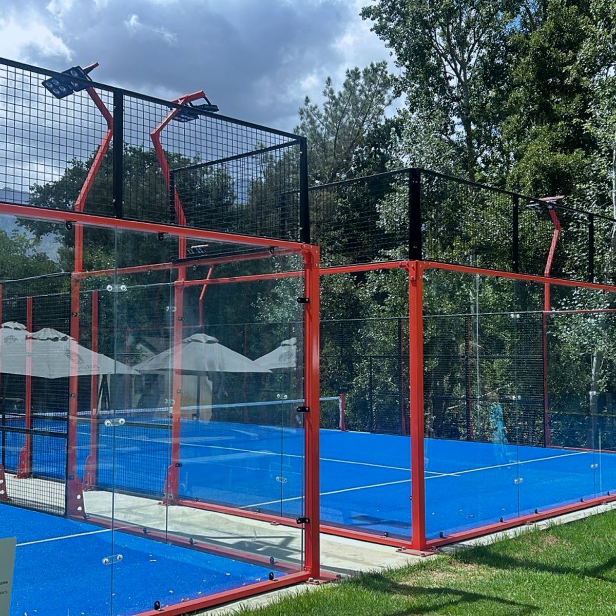 Padel Court im Freien mit roter Stahlkonstruktion und schwarzem Gitter, blauer Kunstrasen