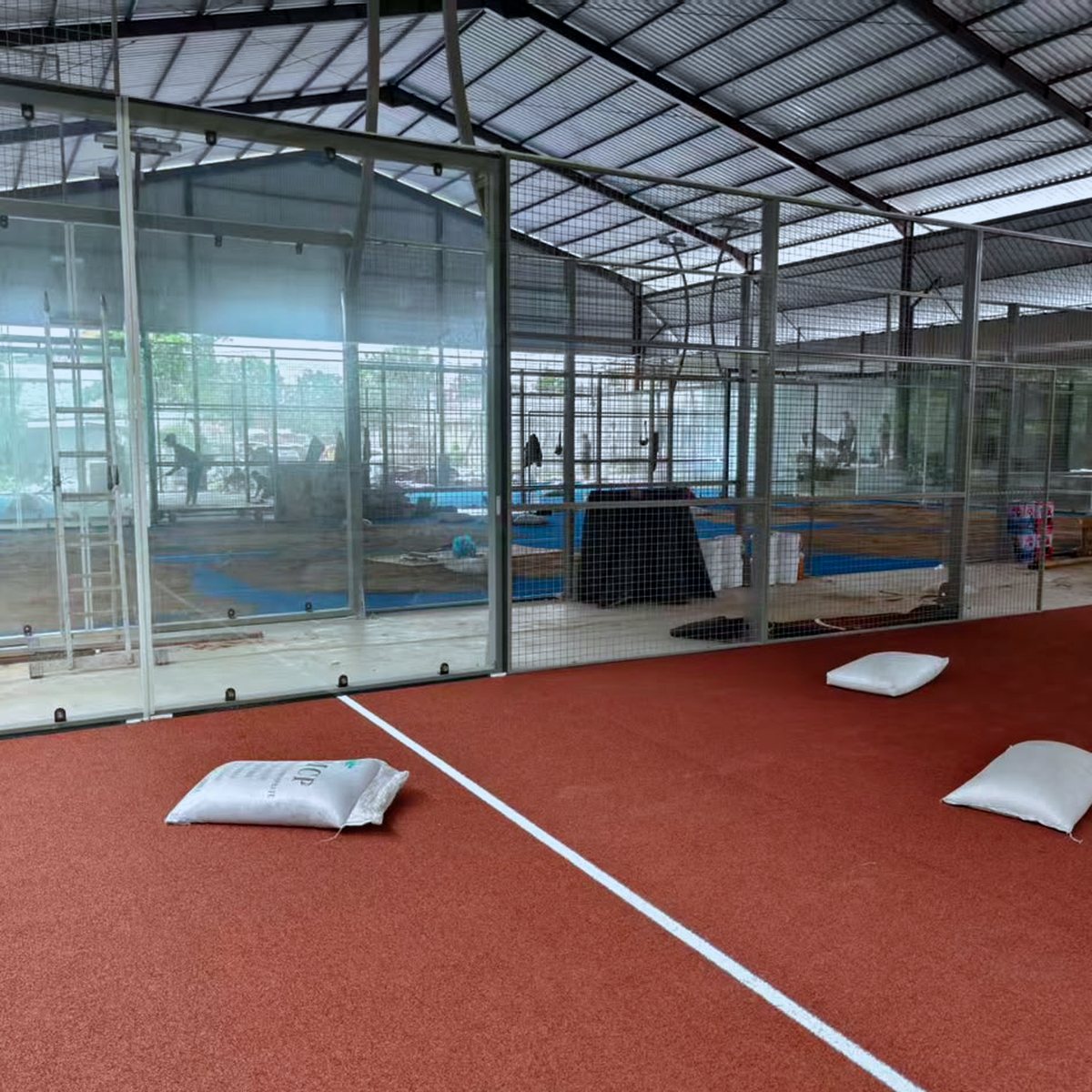 Terrakottafarbener Padel-Kunstrasen wird in einem Glascourt verlegt